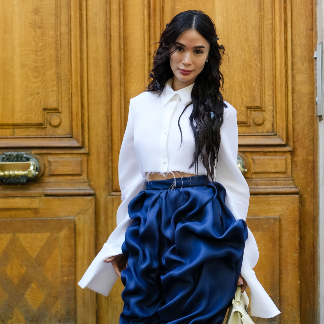 Woman posing in front of a door wearing a white shirt and blue pants. 