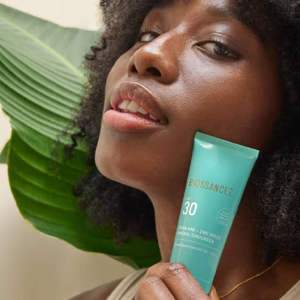 A close up of a woman holding a Biossance sunscreen.