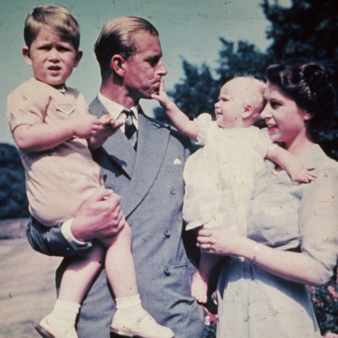 Prince Philip holding Prince Charles while Princess Anne, held by Queen Elizabeth, pulls on his lip