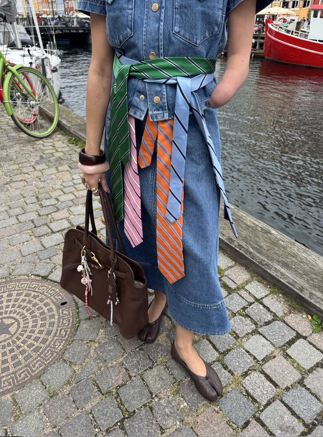 a close up of April Lockhart wearing several ties looped over one another with a miu miu bag